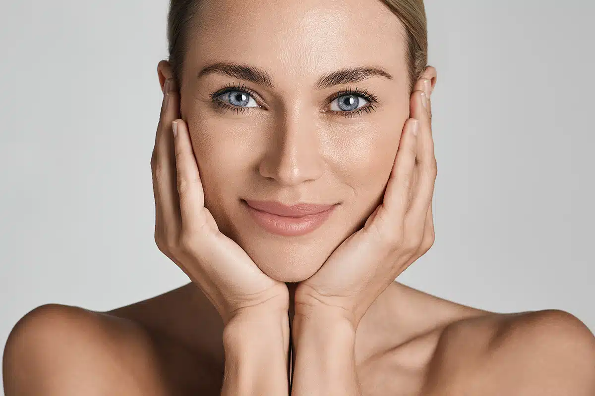 Beautiful woman with healthy facial skin touching hands moisturized face skin