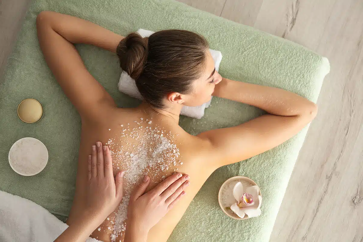 Young woman having body scrubbing procedure with sea salt